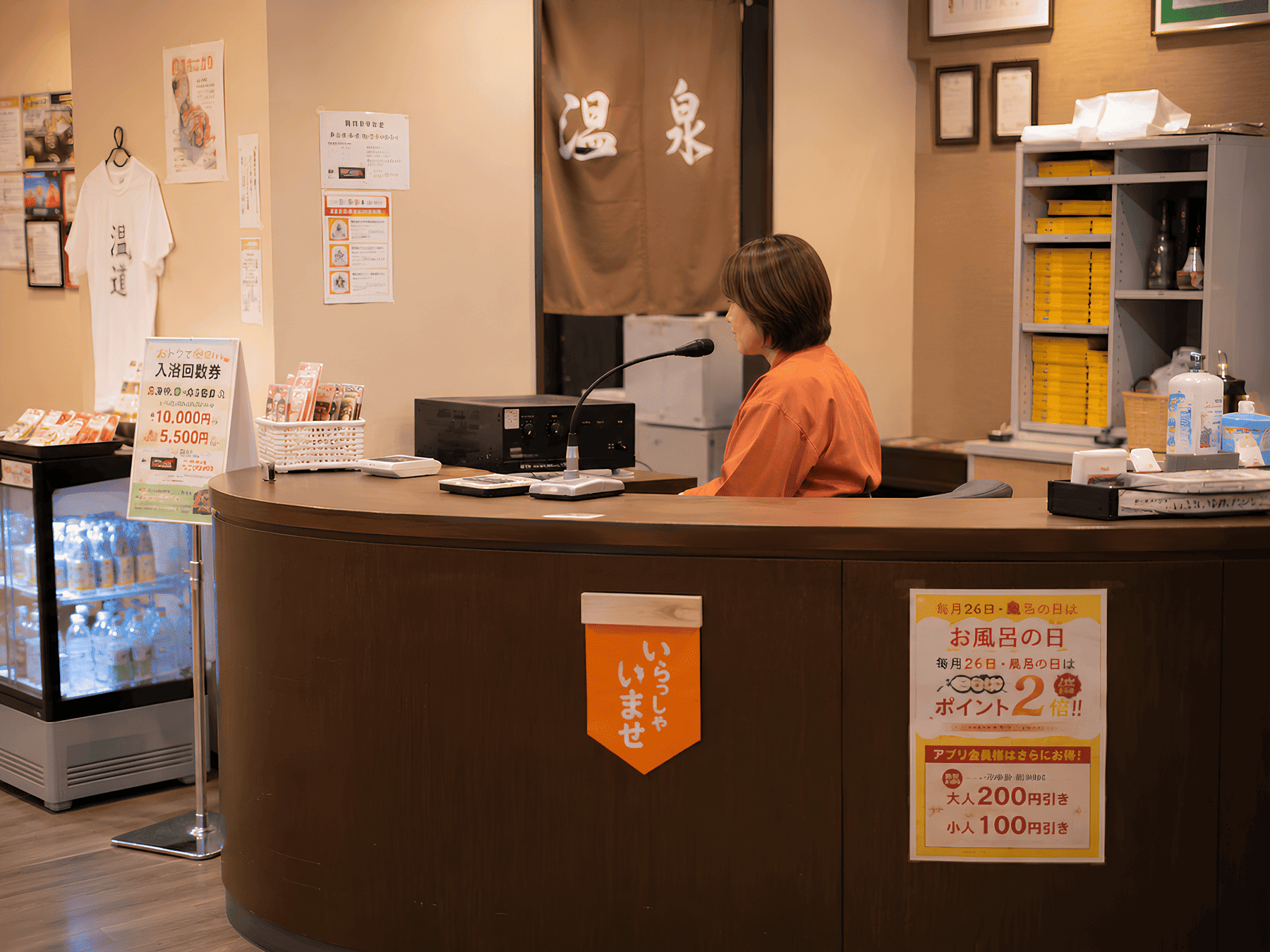 温泉施設のフロント（受付）で、スタッフの女性がマイクに向かって館内アナウンスをしゃっべてる様子。